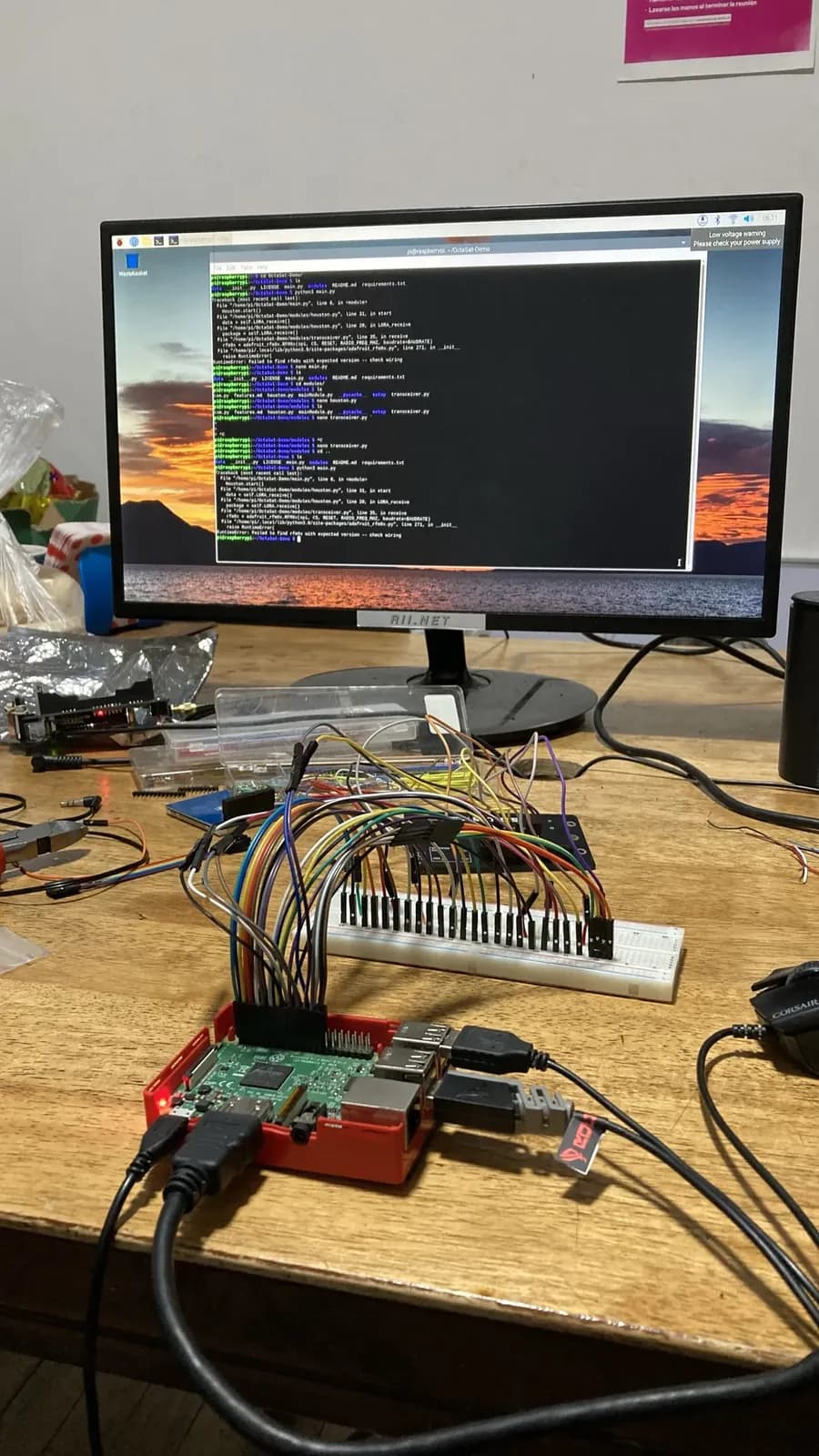 A Raspberry Pi 3 on a breadboard in front of a monitor full of Python tracebacks