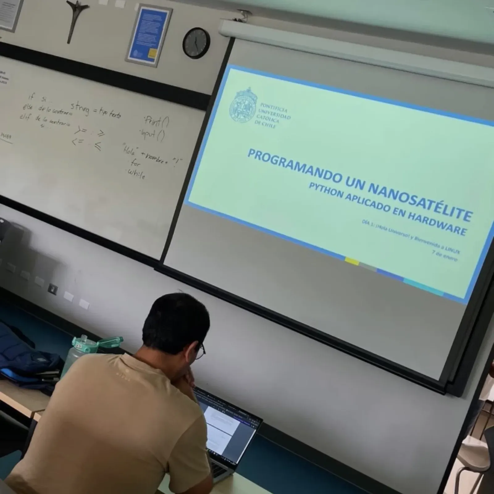 A slide reading Programando un nanosatélite, Python aplicado en hardware, projected in a university classroom next to a whiteboard