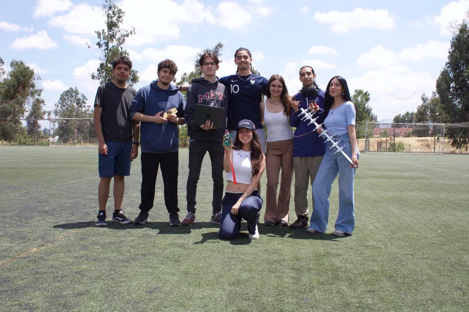 Eight team members on a football field holding a laptop, a flight board and a Yagi antenna